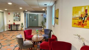 A hotel lobby with red chairs, a table, a mirror, a plant, and a painting on the wall. - Brit Hotel Nantes St Herblain - Le Kerann (Saint-Herblain)