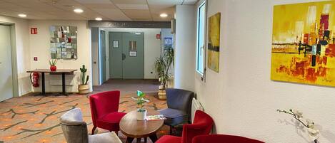 Un hall d’hôtel avec des chaises rouges, une table, un miroir, une plante et un tableau accroché au mur.