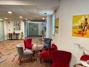Eine Hotelhalle mit roten Stühlen, einem Tisch, einem Spiegel, einer Pflanze und einem Bild an der Wand.