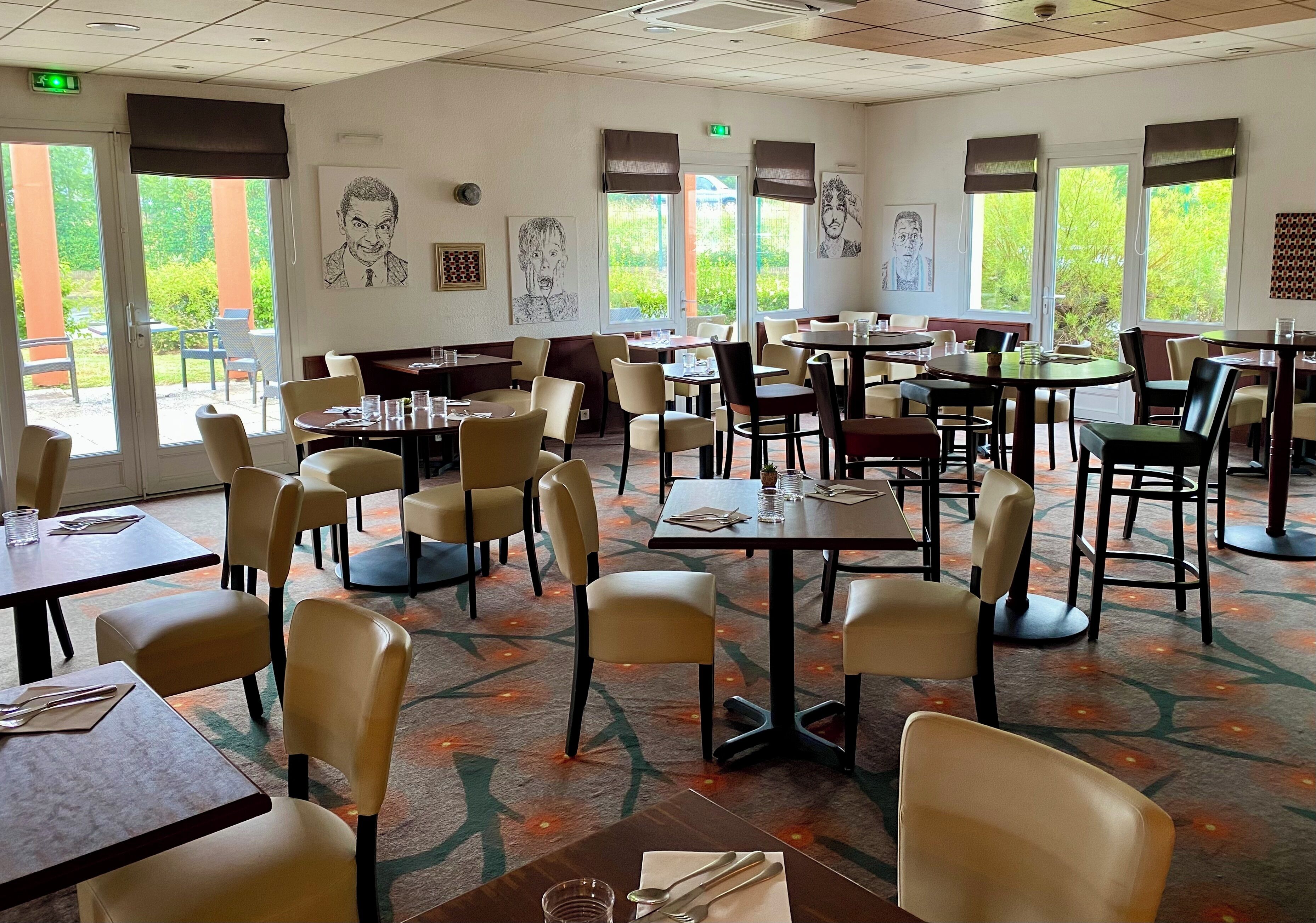 A restaurant with multiple tables and chairs, large windows, and artwork on the walls.