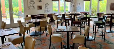 A restaurant with multiple tables and chairs, large windows, and artwork on the walls.