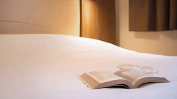 A neatly made bed with a book and glasses on it.