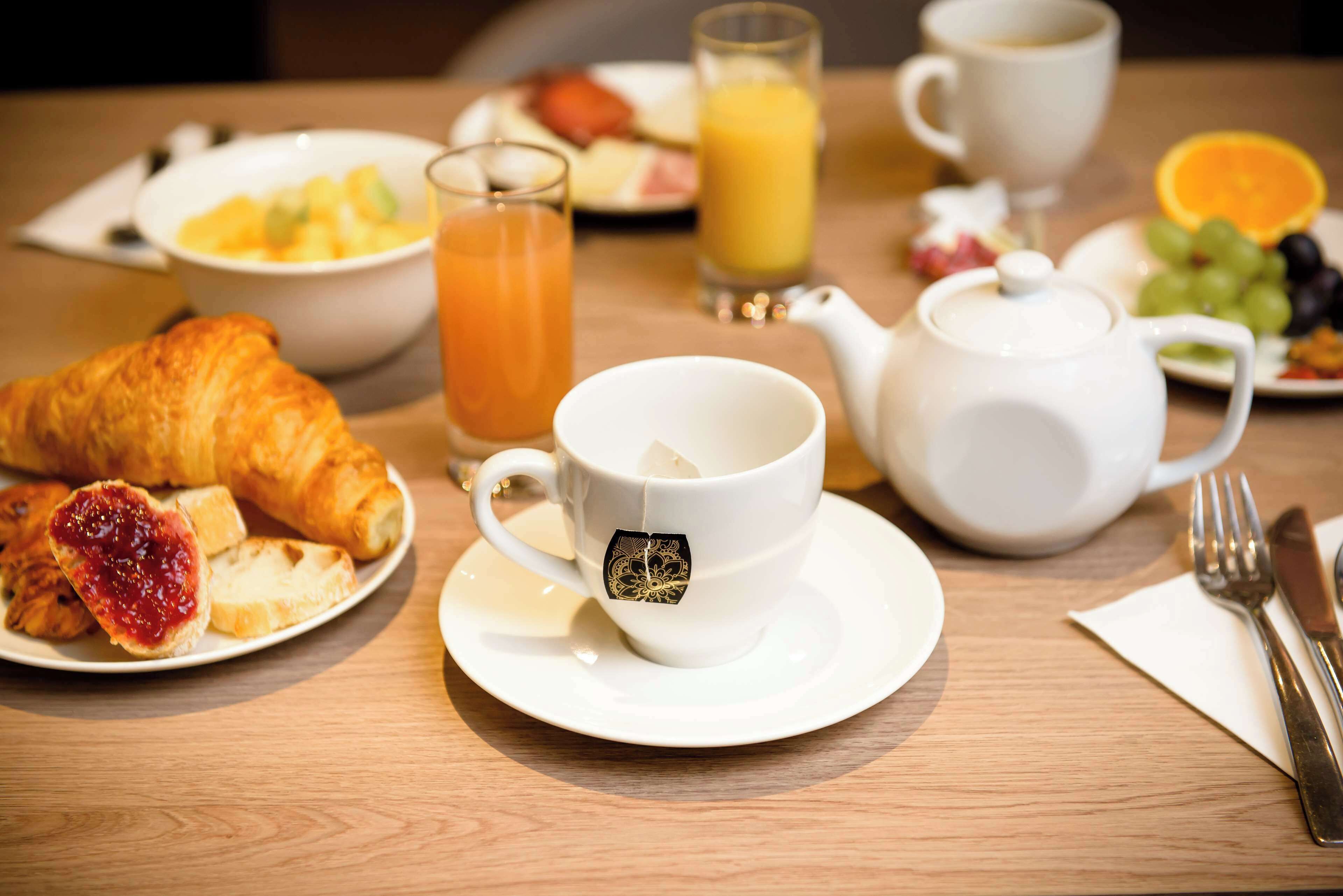 A breakfast setting with croissants, tea, juice, and fruit on a wooden table.