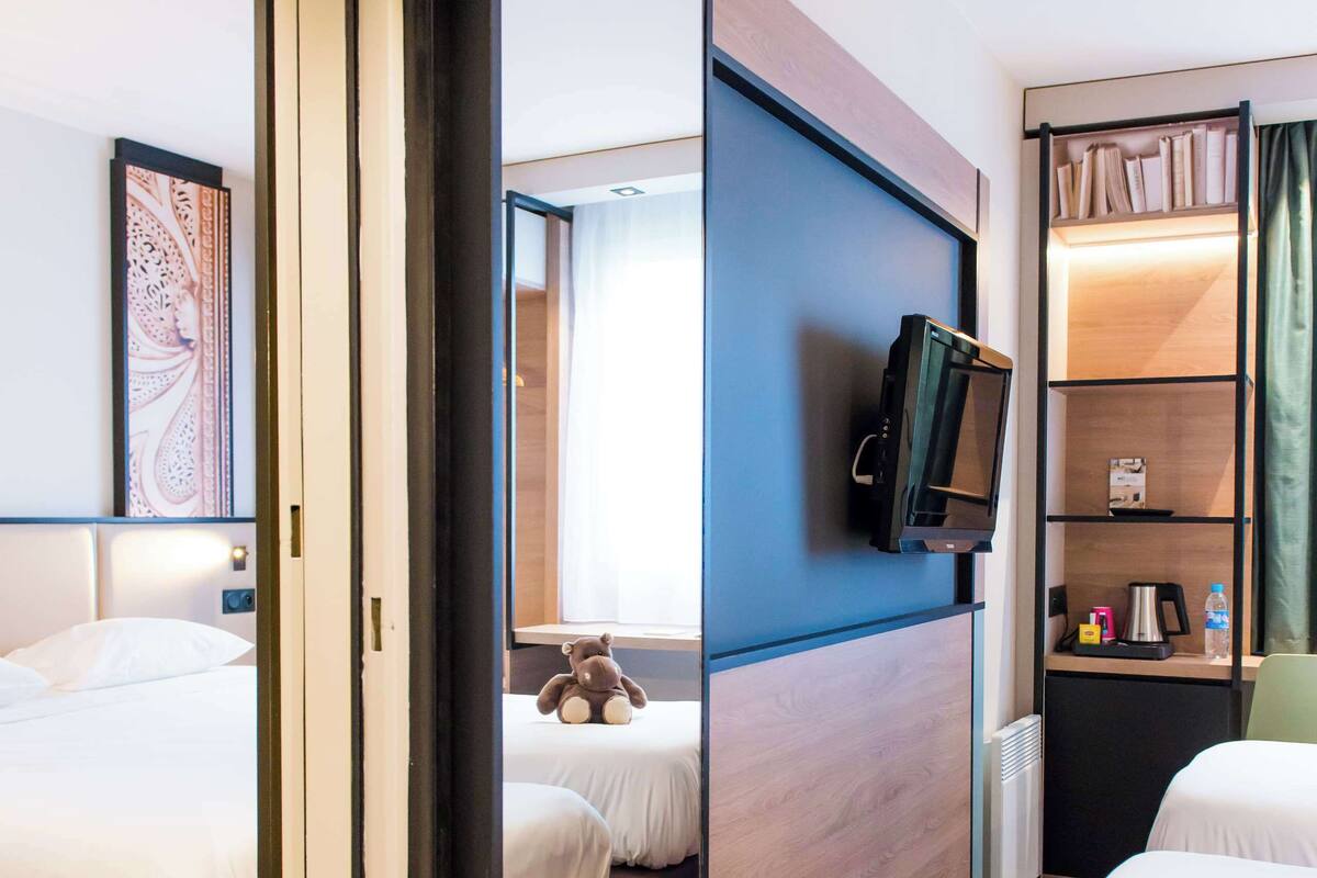 A hotel room with two beds, a television, a desk with a computer, and a bookshelf.