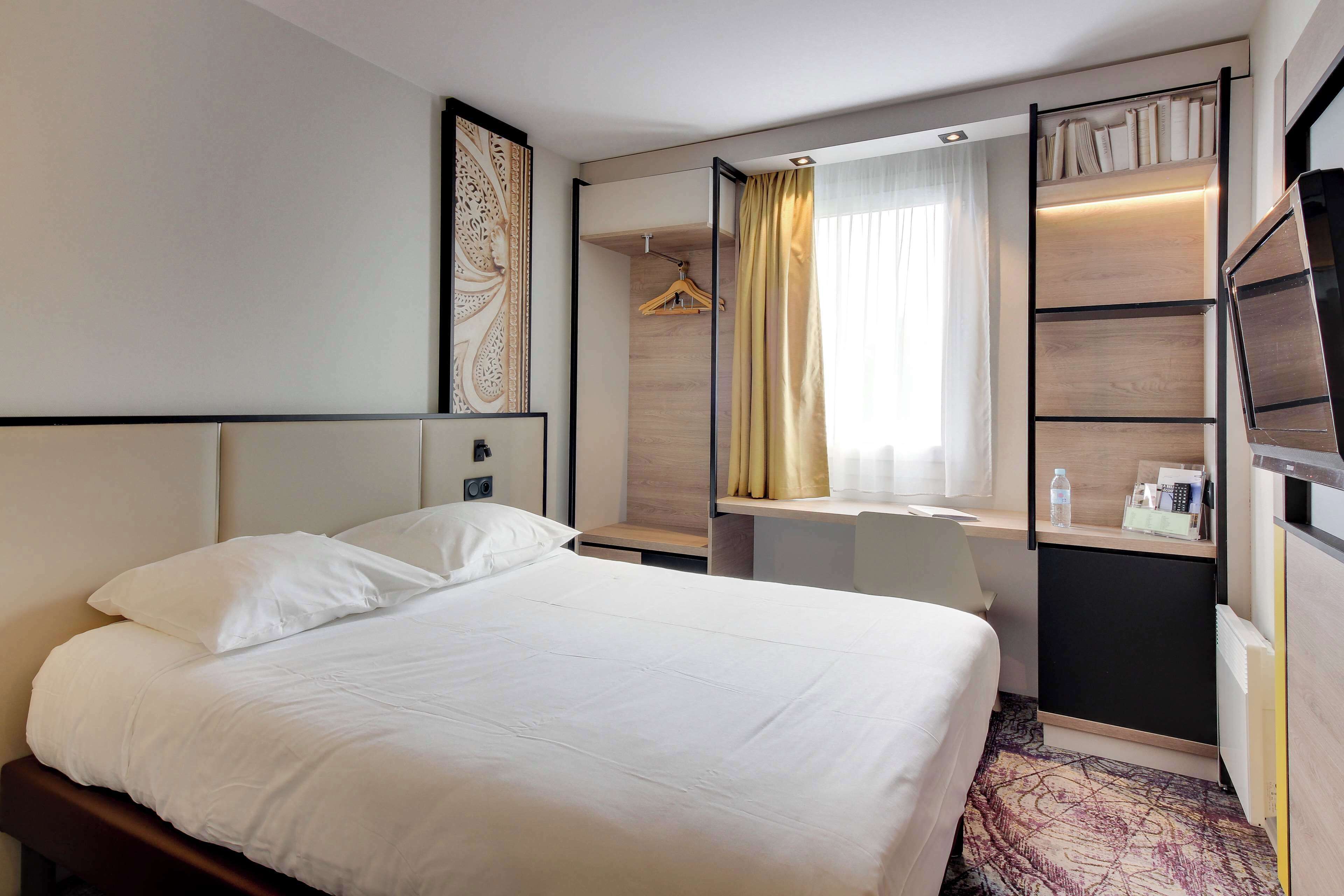 Habitación de hotel con cama, escritorio, armario y zona de ducha.