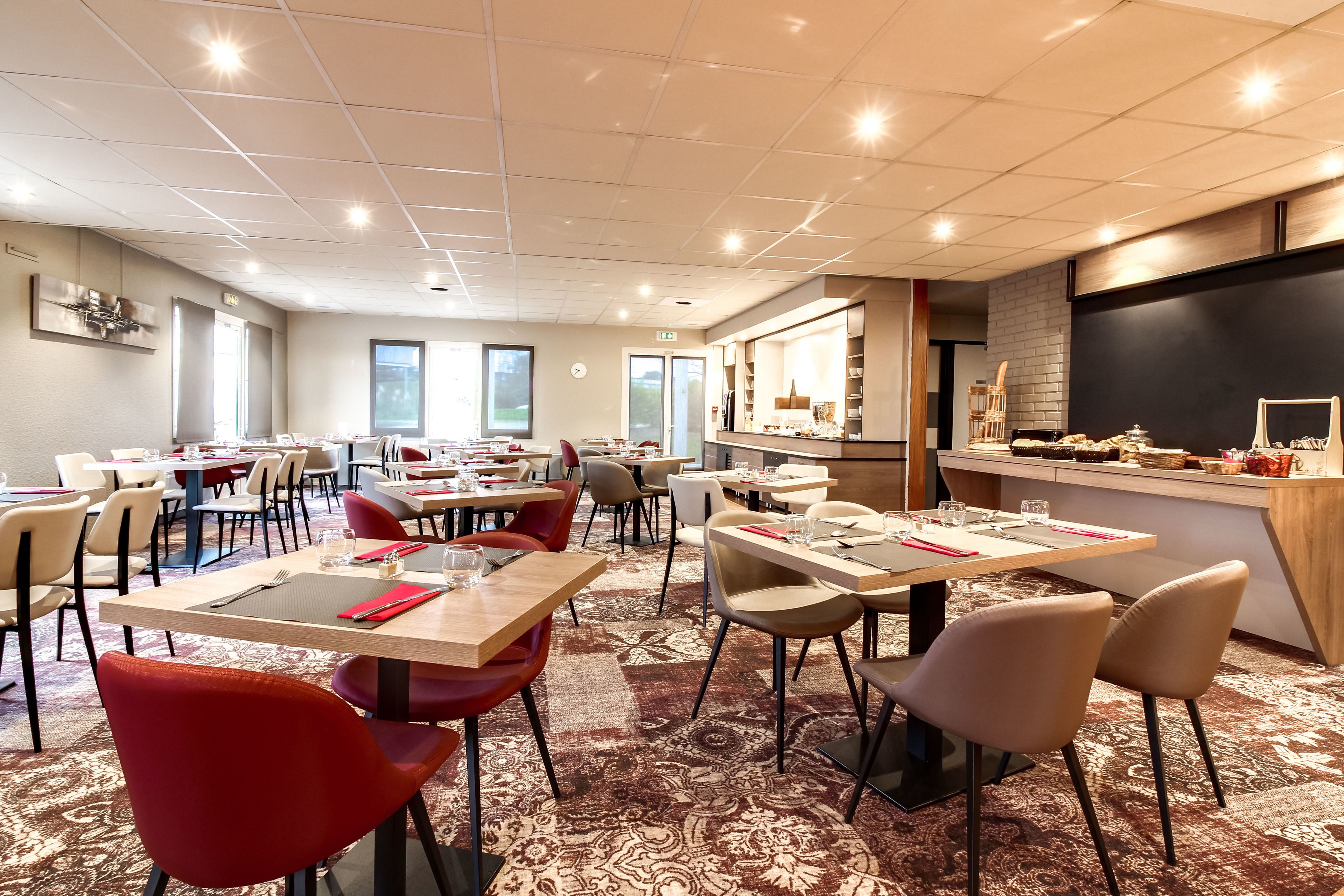 Une salle à manger d’hôtel avec plusieurs tables et chaises, un comptoir de cuisine et une horloge au mur.