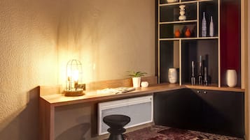 A modern room with a wooden desk, a radiator, a black stool, and a decorative shelf with various items.