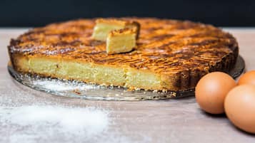 A round cake with a golden-brown crust on a glass plate, dusted with powdered sugar, with two whole eggs beside it.