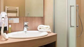 Un baño moderno con tocador de madera, un espejo, un lavabo, una toalla y una ducha con mampara de vidrio.