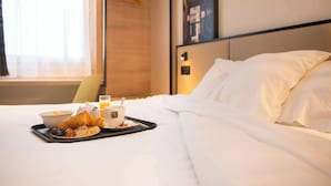 A neatly made bed with white linens, a tray with croissants, a bowl of fruit, and a cup of coffee on a hotel room table. - Brit Hotel Brest Le Relecq Kerhuon (Le Relecq-Kerhuon)