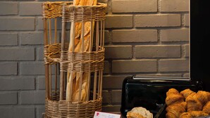 A bakery display with baguettes, croissants, and a loaf of bread on a wooden board, set against a brick wall with hanging pendant lights. - Brit Hotel Brest Le Relecq Kerhuon (Le Relecq-Kerhuon)