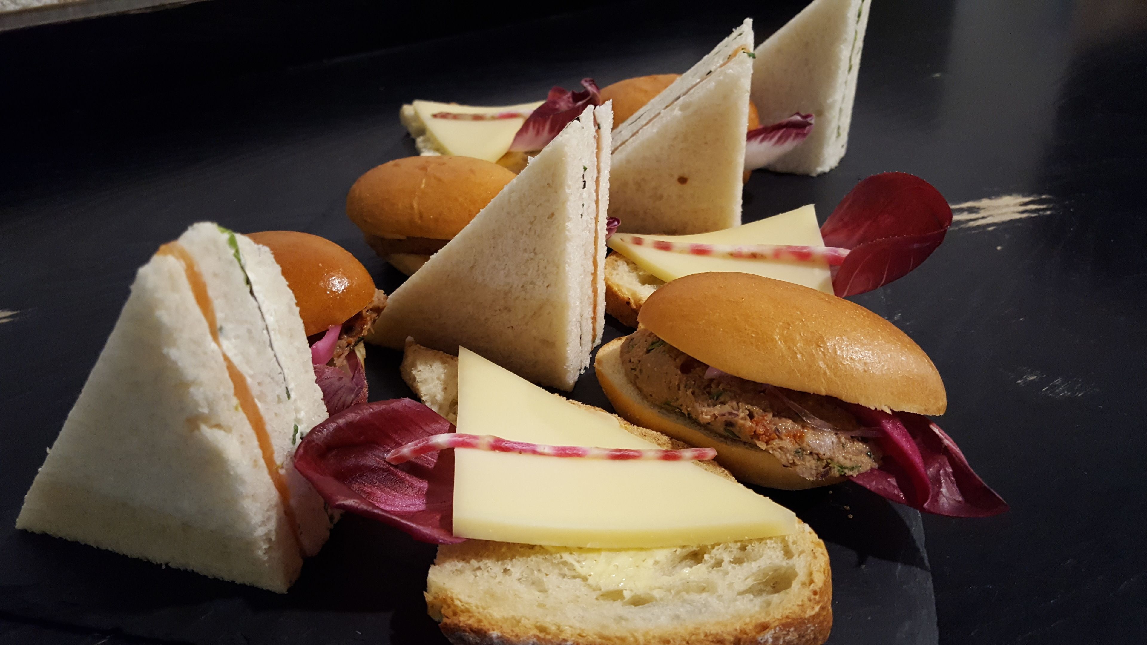 Variedad de sándwiches y pequeñas pastas sobre un plato oscuro.