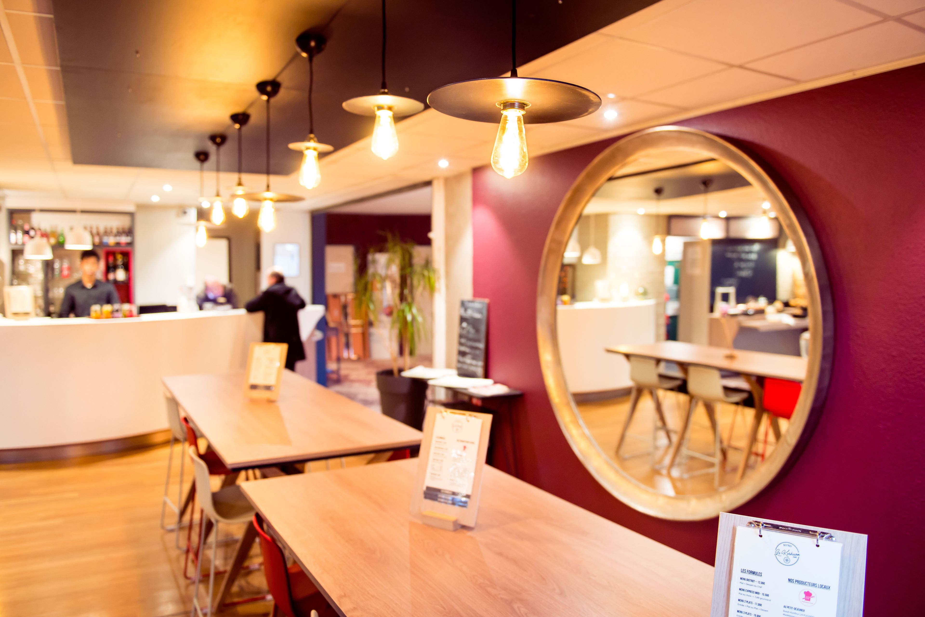 Ein Restaurantinneres mit Holztischen, hängenden Glühbirnen und einem großen Spiegel an der Wand.