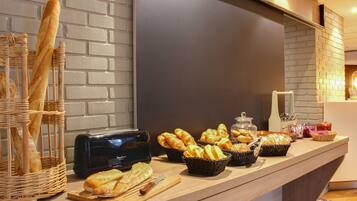 A buffet counter with various breads and pastries, a toaster, and baskets of food.