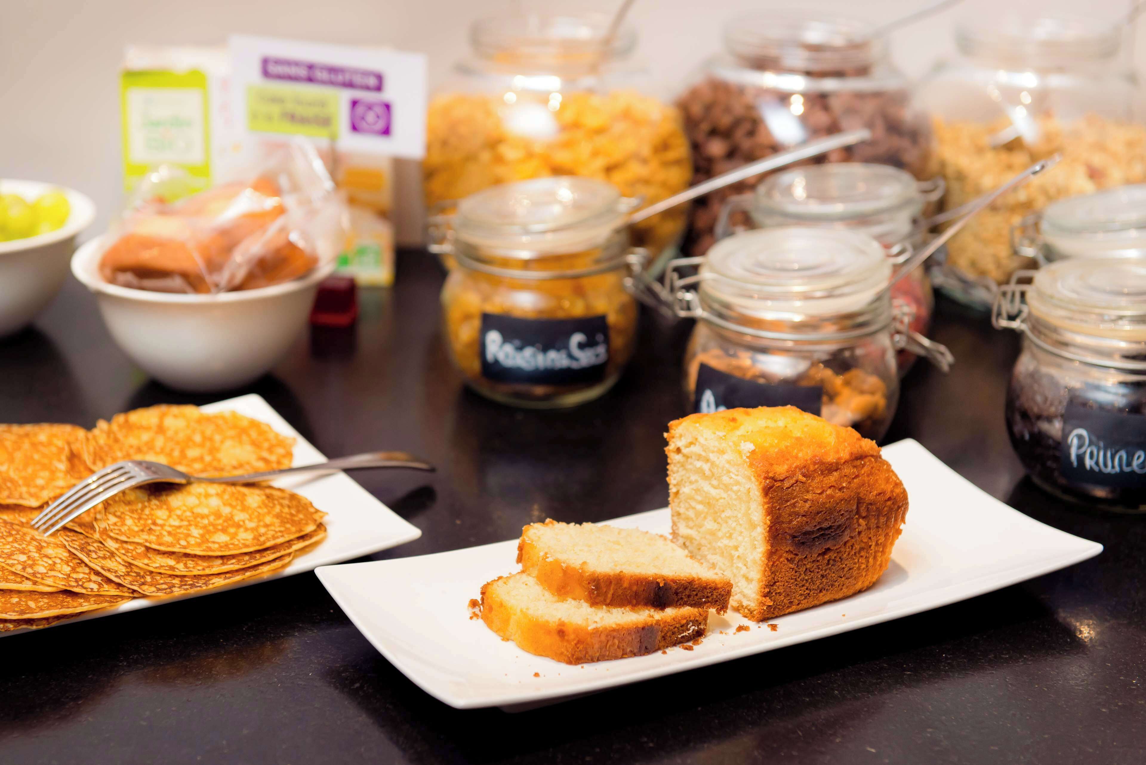 Una mesa de buffet con diversos alimentos, como panqueques, una rebanada de pastel y frascos con salsas.