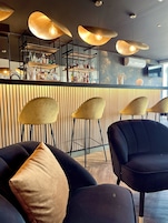 Un área de bar con un revestimiento de listones de madera, varios taburetes y una variedad de botellas en estanterías.