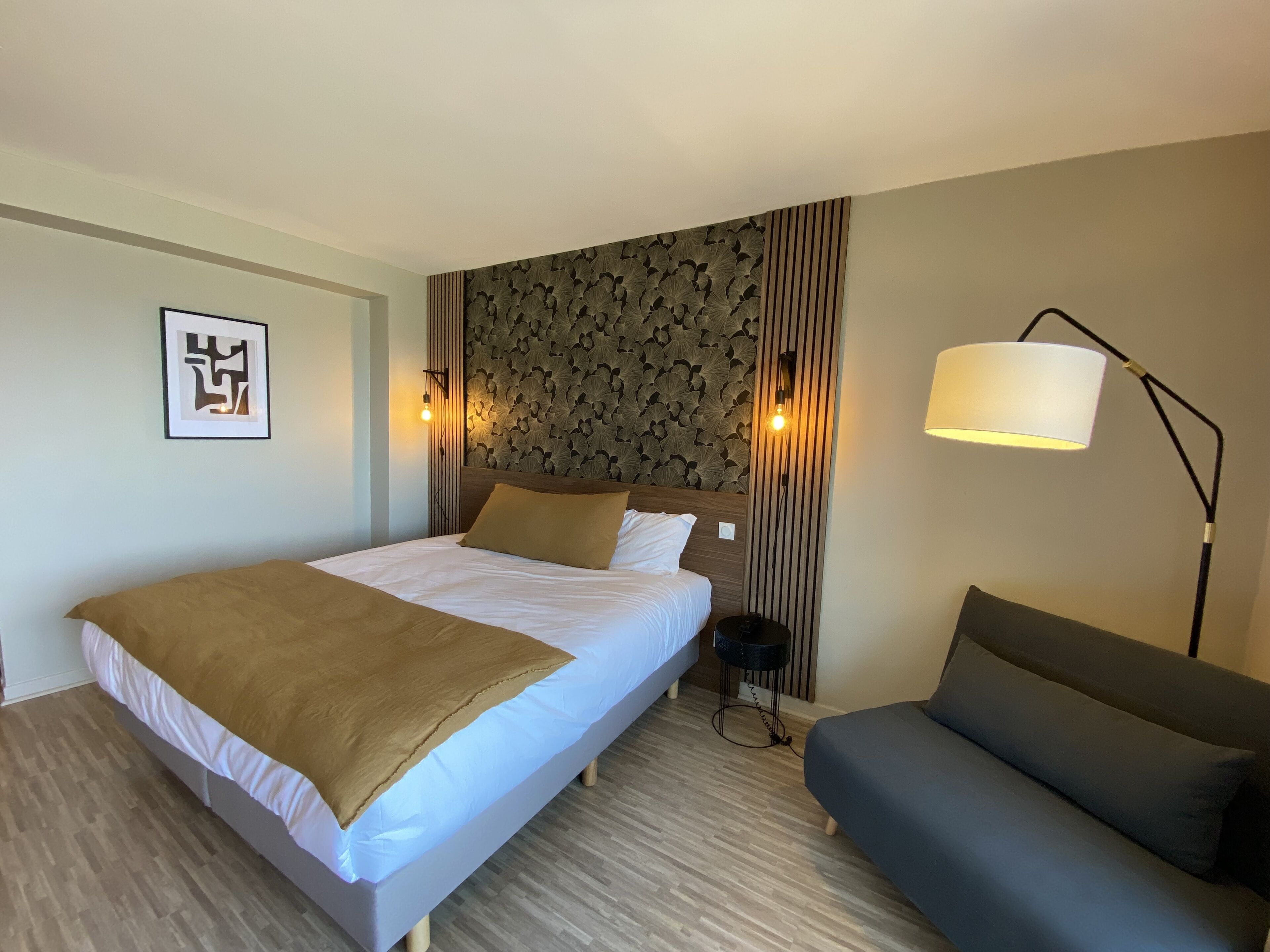Ein Hotelzimmer mit einem Bett, einer Couch, einer Wandlampe und einem gerahmten Bild.
