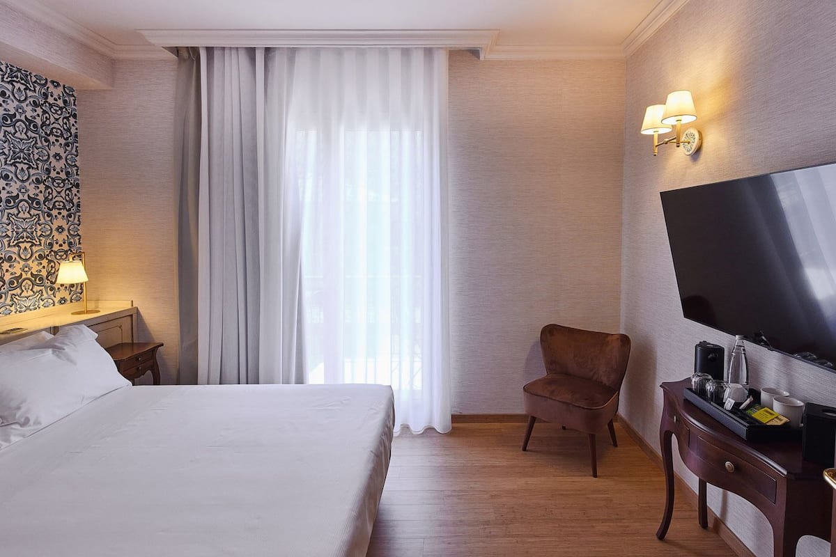 A hotel room with a bed, a chair, a TV, and a desk with a lamp.