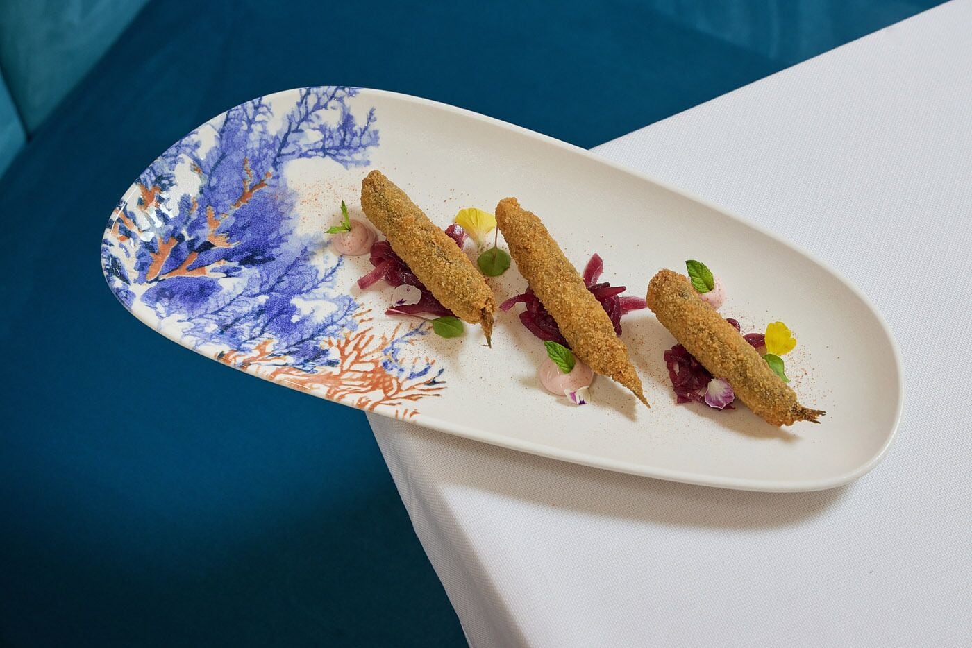 Une assiette blanche contenant trois aliments panés et quelques légumes, posée sur une table.