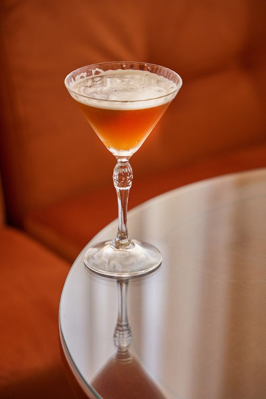 A cocktail in a martini glass on a reflective surface.