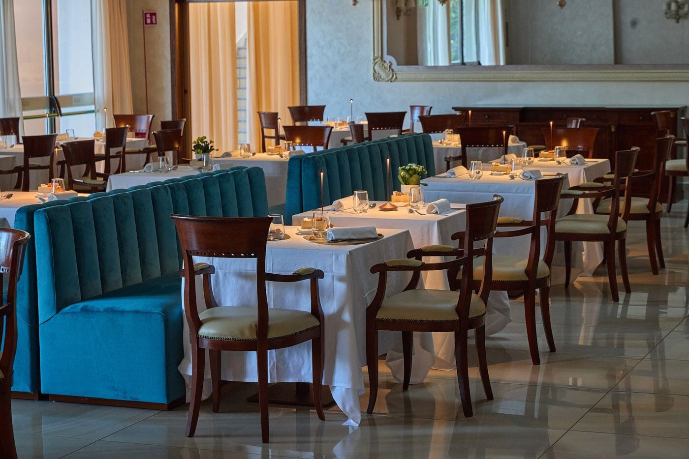 Un comedor formal con mesas largas, sillas y un banco tapizado en color aguamarina.