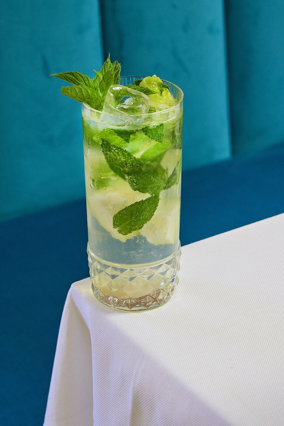 Un verre transparent rempli de glaçons et de feuilles de menthe, posé sur une nappe blanche.