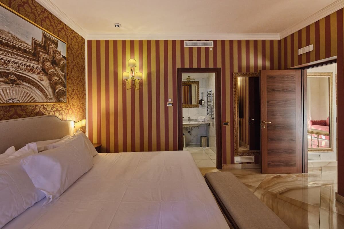 A hotel room with a large bed, a bathroom with a mirror, and a door leading to another room.