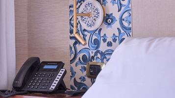 Une chambre d’hôtel avec un lit, une table de chevet avec un téléphone, une lampe et un mur recouvert d’un papier peint à motifs bleus et blancs.