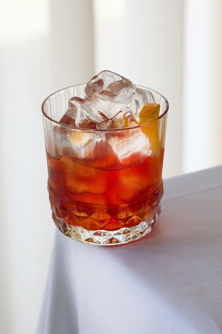 A clear glass with ice cubes and a slice of orange in a textured glass.