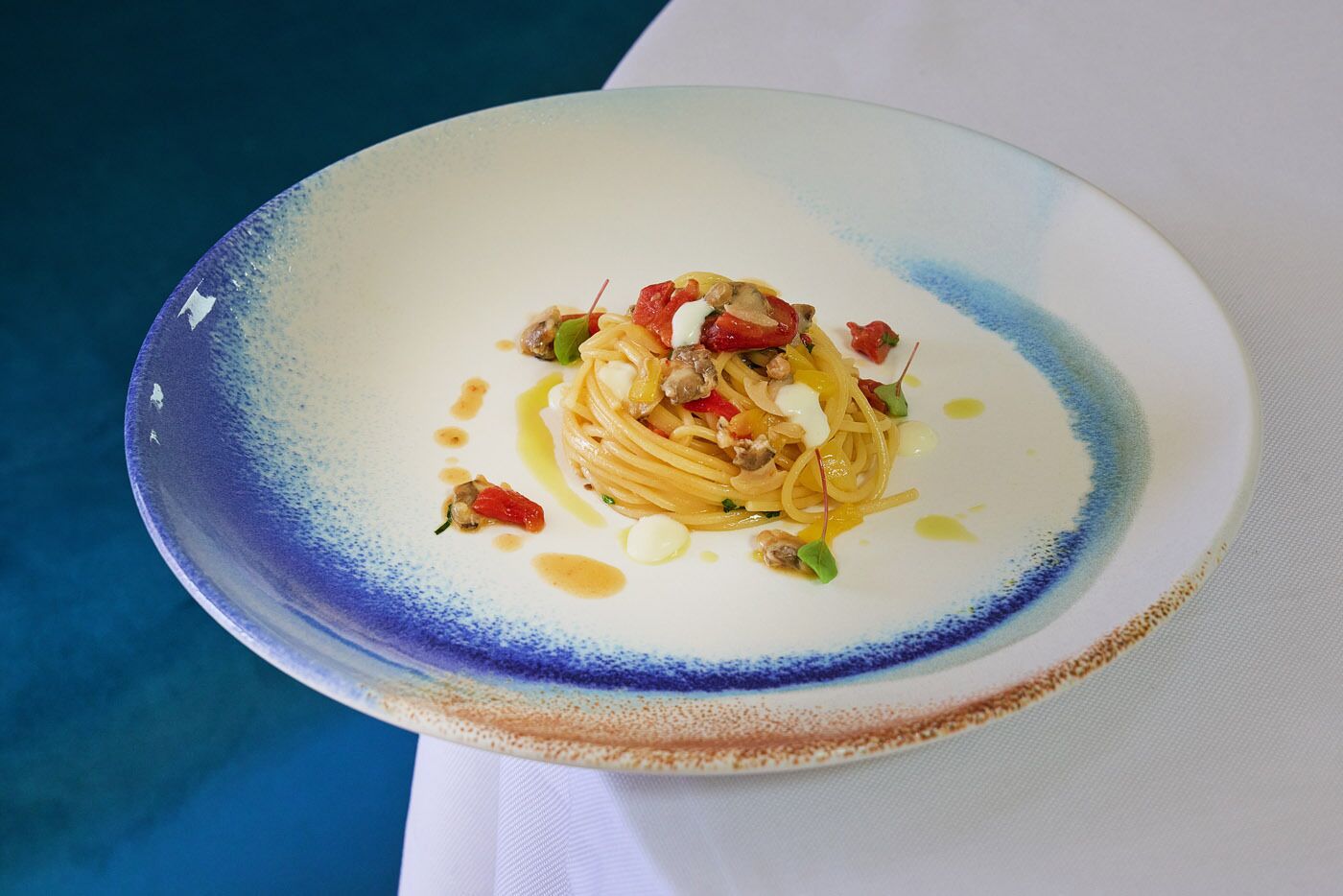 A plate of pasta with a blue rim, placed on a white tablecloth.
