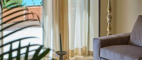 A living room with a sofa, a lamp, a coffee table with decorative items, and a view of a pool through sheer curtains.
