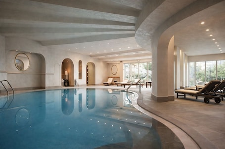 An indoor swimming pool with lounge chairs and a sunbed area.. Quiete Taormina Naxos, Tapestry Collection by Hilton