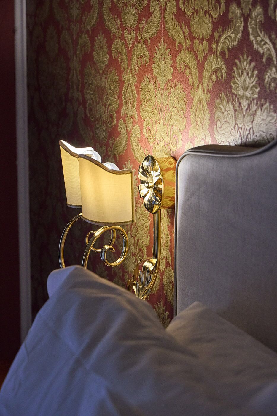 A bed with a headboard, a bedside lamp, and a wall with ornate wallpaper.
