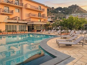 Ein Hotel mit Swimmingpool, Liegestühlen und Blick auf einen Hügel.