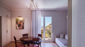 A dining area with a round table and chairs, a chandelier, a painting, and a view of the sea through a sliding door.