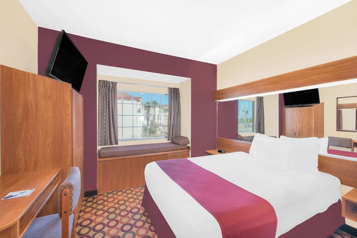 Een hotelkamer met een groot bed, een raam met uitzicht, een bureau en een aan de muur bevestigde televisie.