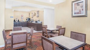 Une salle à manger d’hôtel avec des tables et des chaises, une cuisine en arrière-plan et une œuvre d’art encadrée au mur.