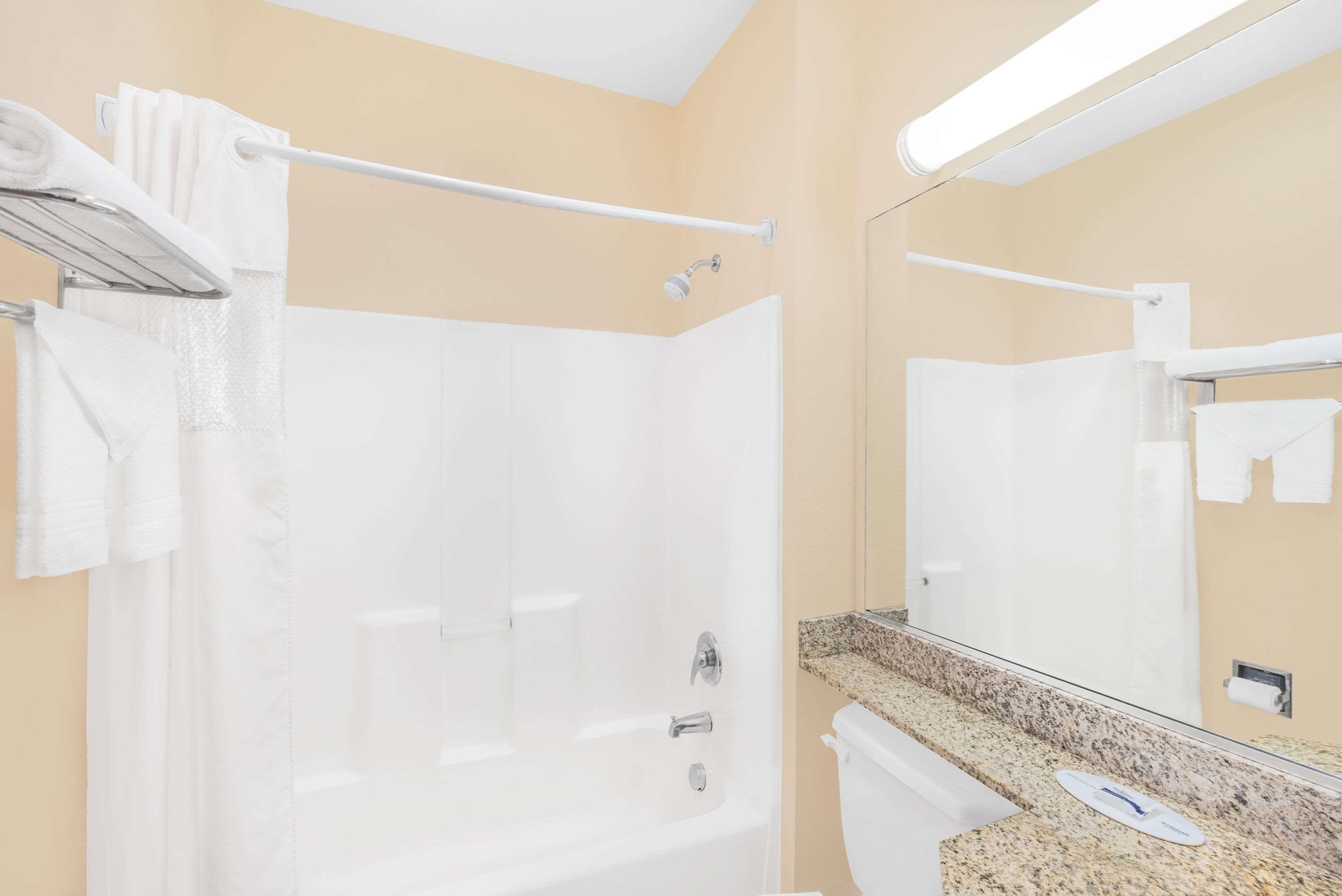 Un baño de hotel con bañera, inodoro, lavamanos con encimera y espejo.