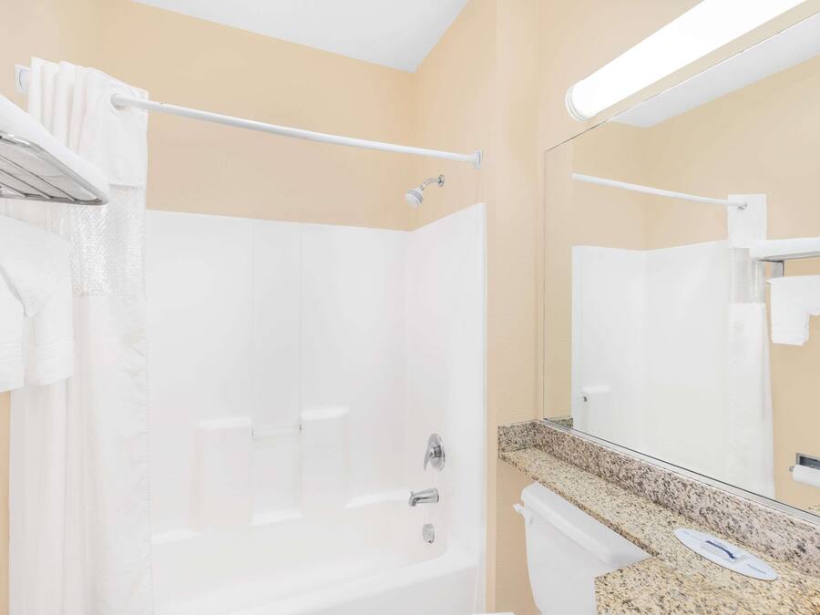 A hotel bathroom with a bathtub, a toilet, a sink with a countertop, and a mirror.