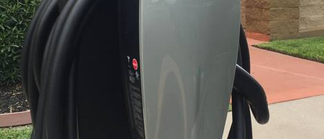 Une borne de recharge, reliée à un câble, est installée devant un bâtiment surmonté d’un dôme et d’une lanterne.
