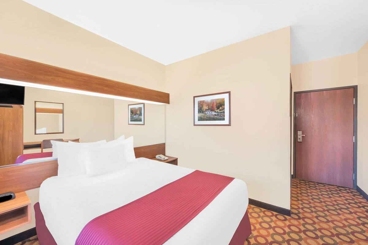 Een hotelkamer met een groot bed, een houten hoofdbord, een nachtkastje met een telefoon, een spiegel en twee ingelijste foto's aan de muur.