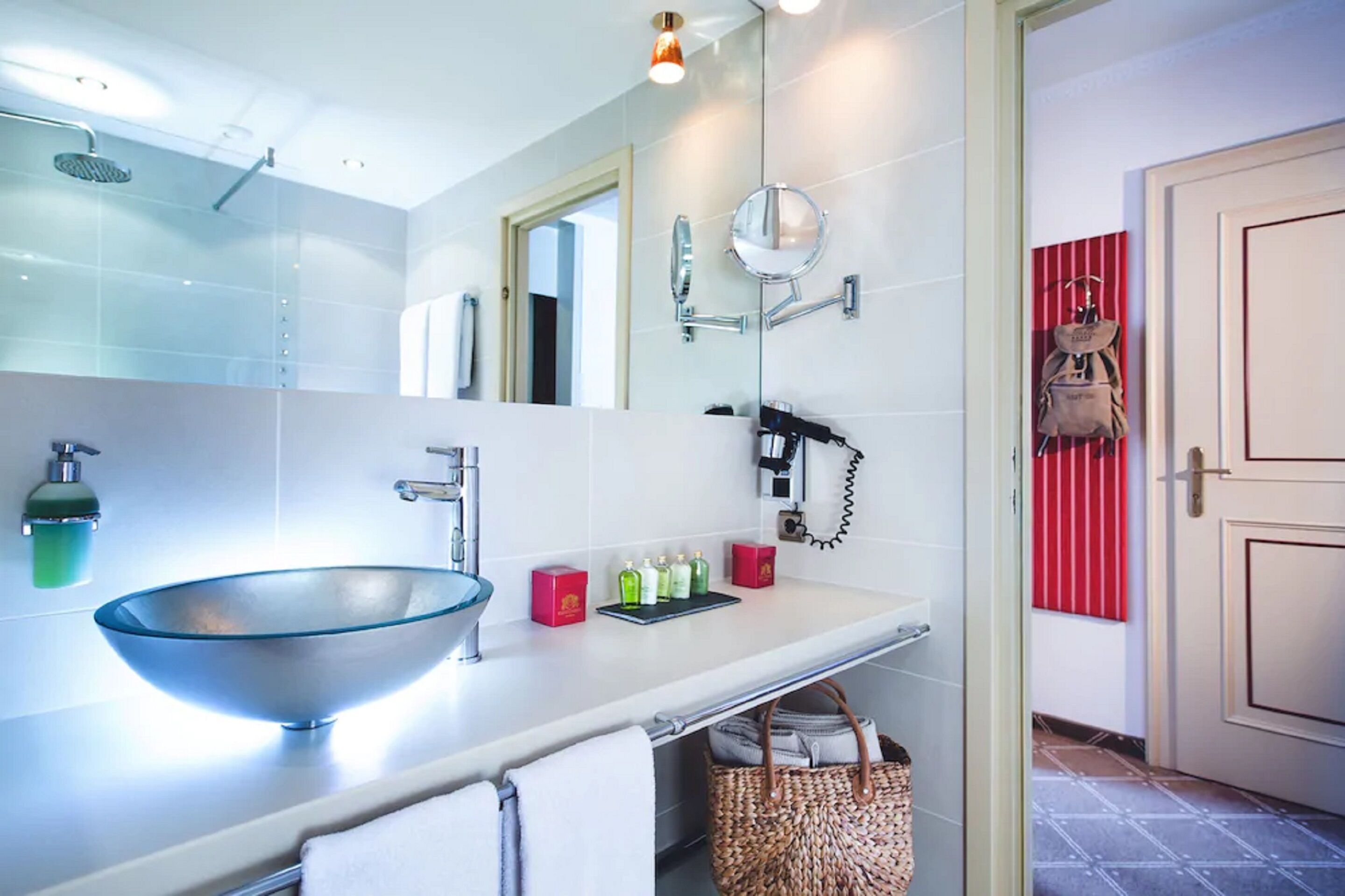 A modern bathroom with a glass bowl sink, a handheld showerhead, a large mirror, and a red-striped towel rack.