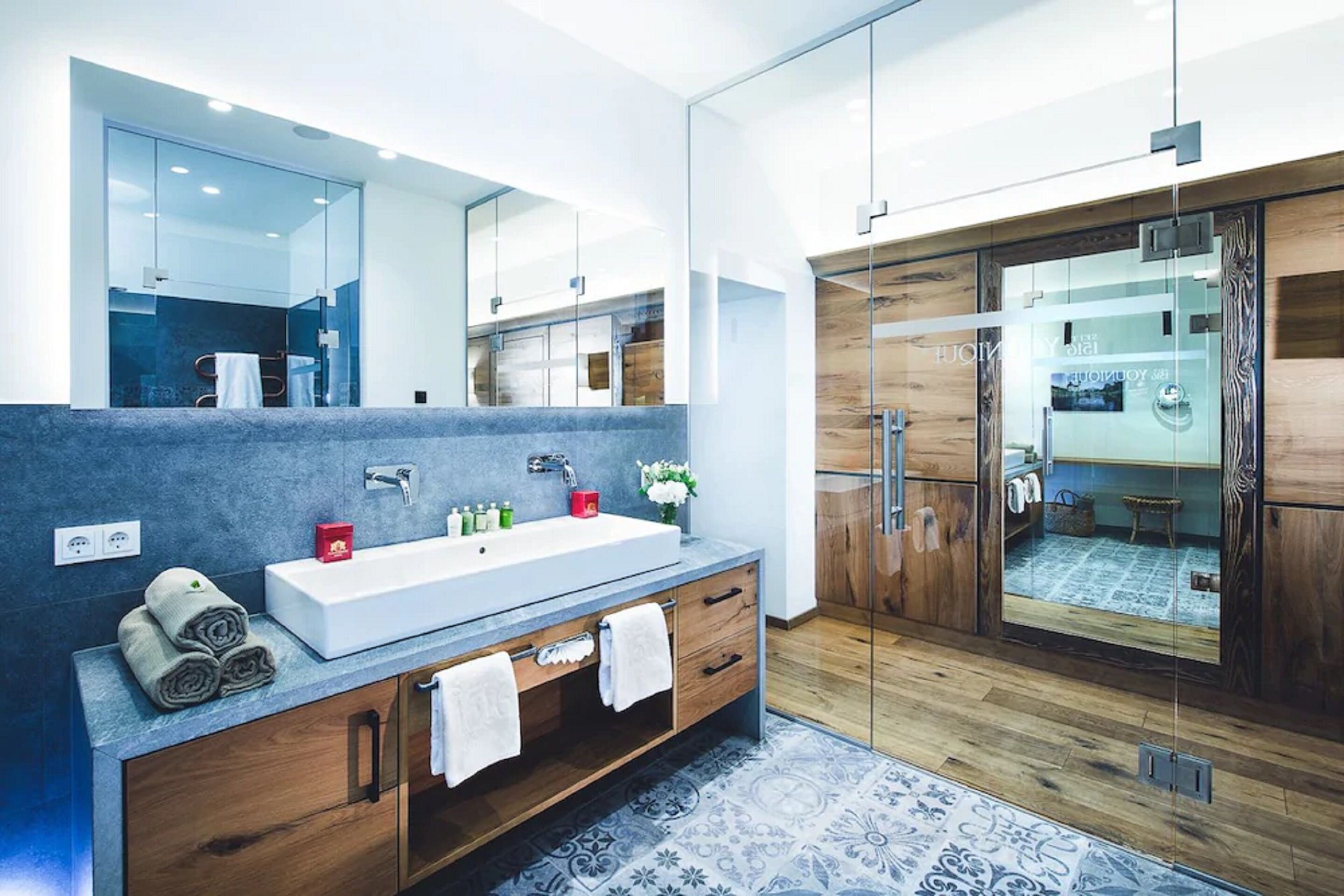 Een moderne badkamer met een grote spiegel, een lang aanrecht, houten kasten en een douchecabine van glas.
