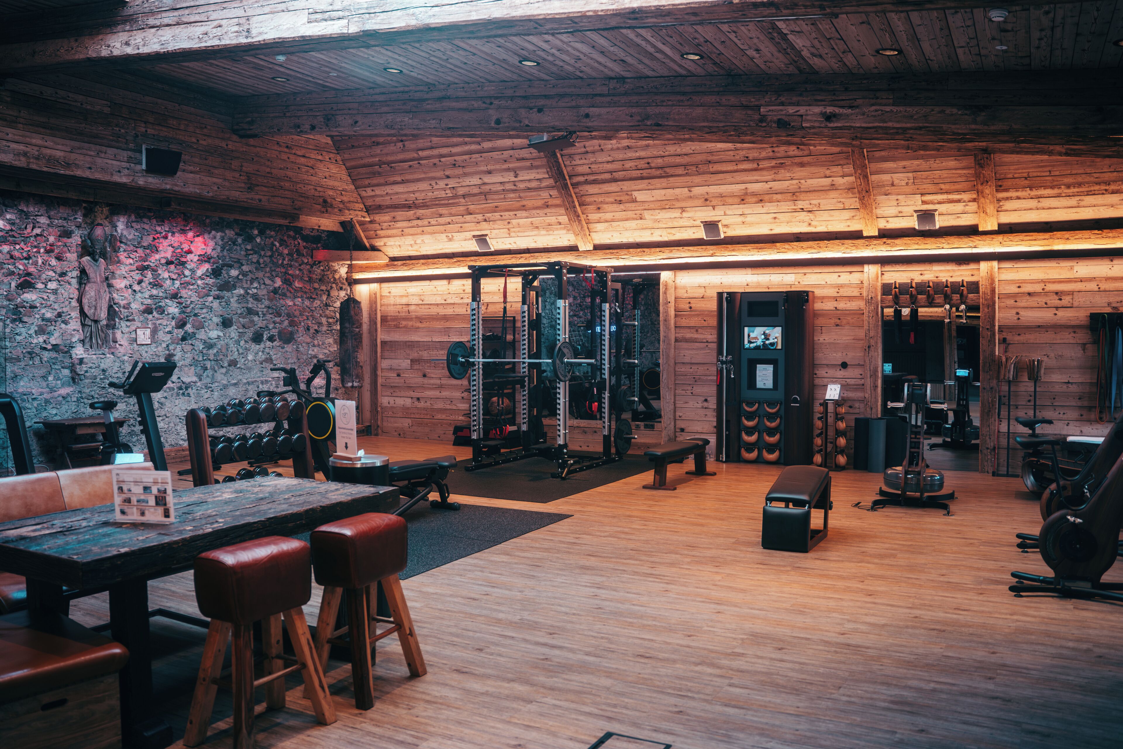 Ein Fitnessraum mit Holzwänden, einer Steinwand und verschiedenen Trainingsgeräten.