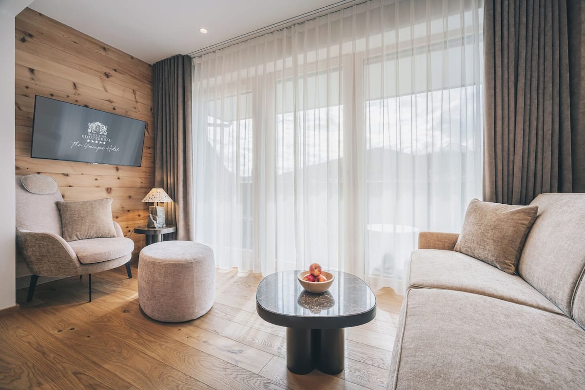 A modern living room with a wooden wall, a flat-screen TV, a sofa, a chair, a round coffee table, and a lamp.