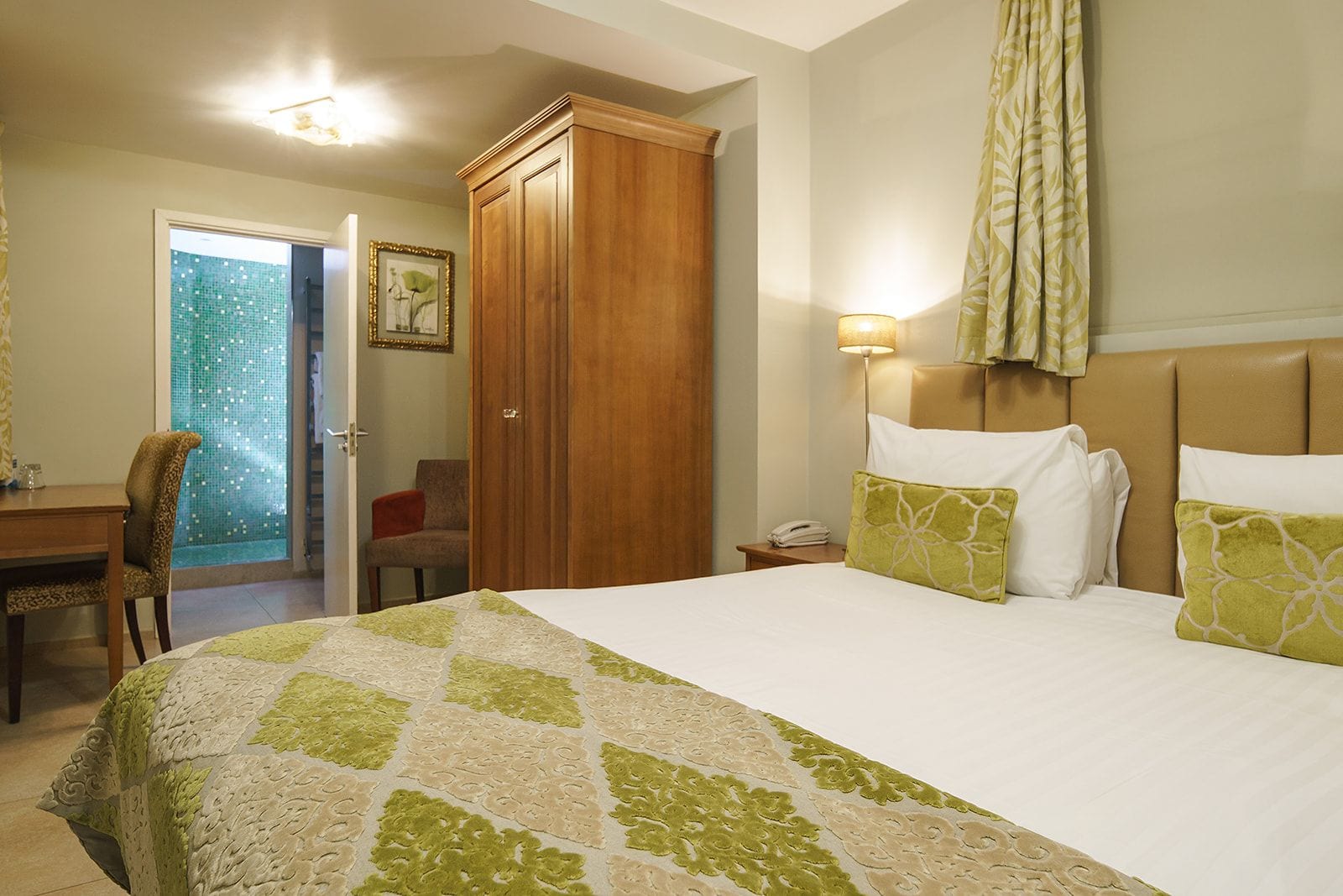 A hotel room with a bed, a desk, a chair, a wardrobe, and a bathroom with a shower.