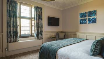 A hotel room with a large bed, a window with curtains, a flat-screen TV, and artwork on the wall.
