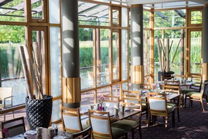 Un restaurant doté de grandes fenêtres, de meubles en bois et offrant une vue sur un plan d’eau.