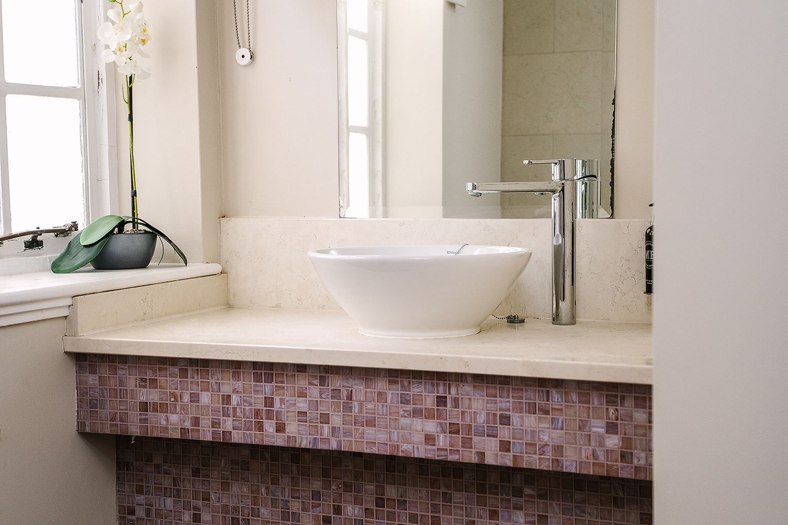 A bathroom with a white sink, a mirror, and a potted orchid.