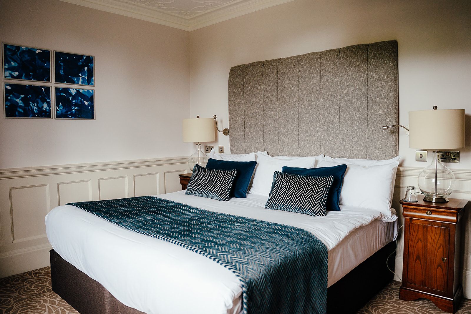 A hotel room with a large bed, two bedside tables, a headboard, and a wall-mounted lamp.